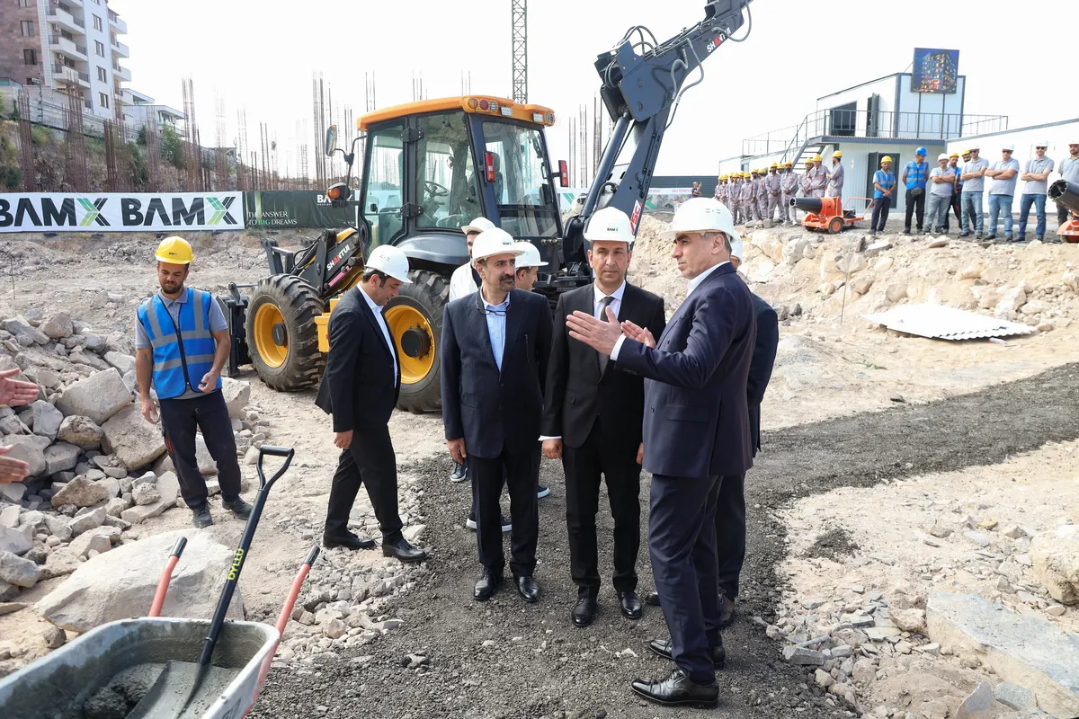 Managers and engineers walking the Nork site past an excavator, Yerevan